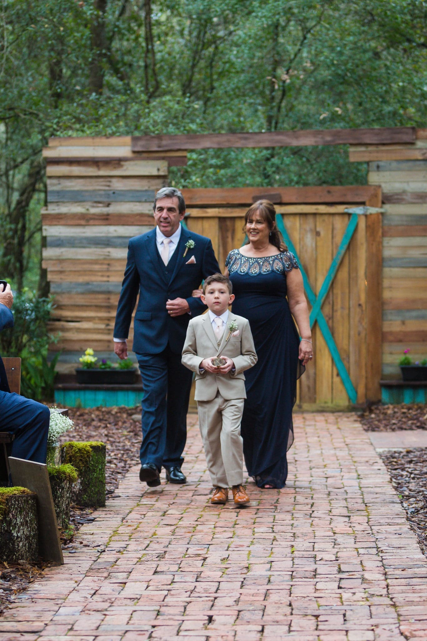 Mother and father of the groom walking down the aisle with the ringbearer and son of the groom.